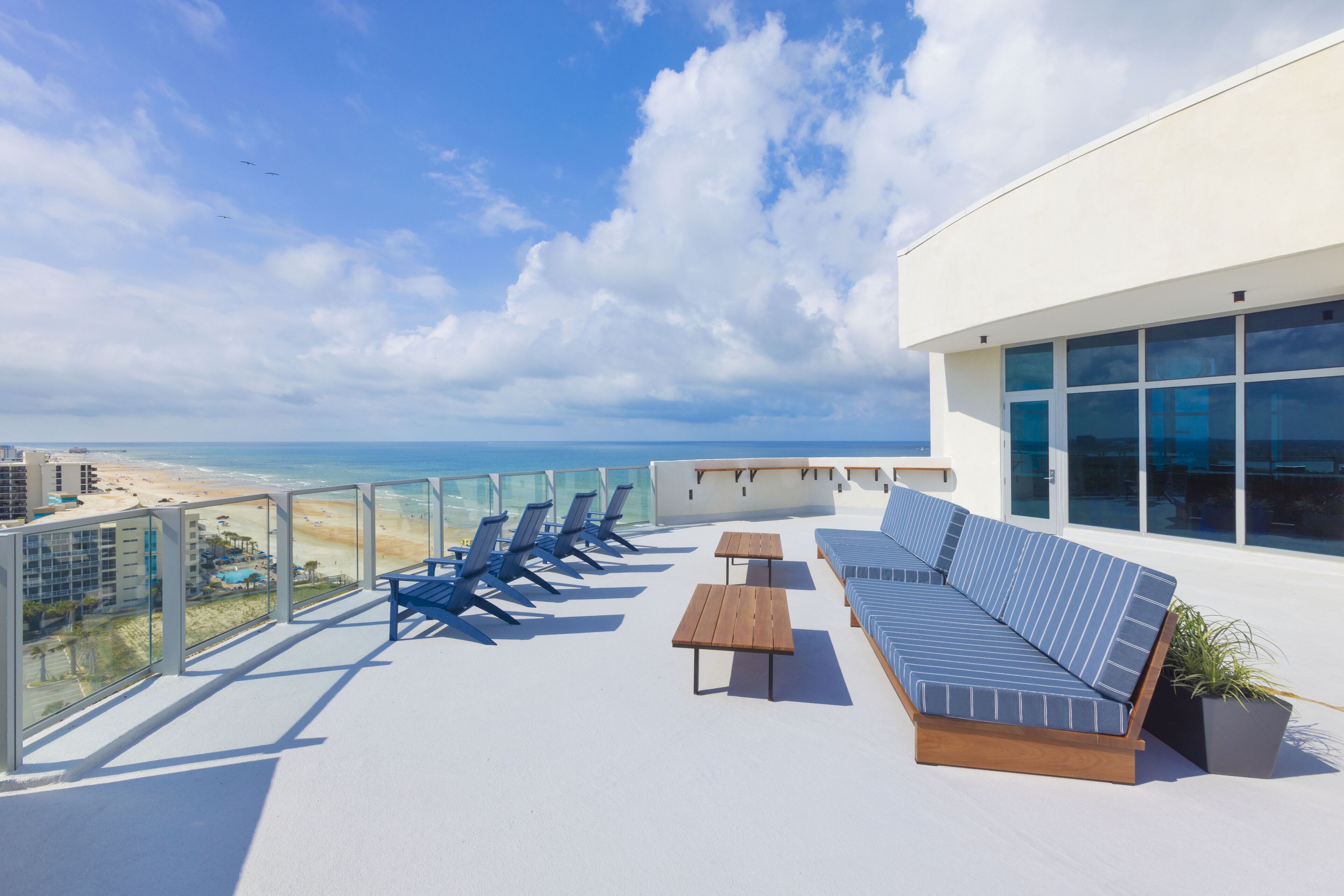 A rooftop terrace with a view of the beach, lounge chairs, a sofa, and a table.