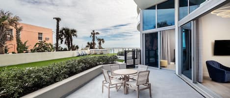A modern outdoor patio with a round table and chairs, a flat-screen TV, and a view of palm trees and buildings.