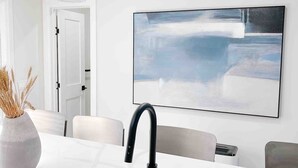 Eine moderne Küche mit weißer Arbeitsplatte, Spüle aus Edelstahl und einem schwarzen Wasserhahn. Über der Spüle hängen zwei Pendelleuchten mit klaren Glaskugeln. Auf der linken Seite der Arbeitsplatte steht eine Vase mit Trockenblumen.