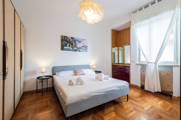 A bedroom with a bed, bedside tables, a painting, a mirror, and a window with curtains. - Riverview Luxury Flat (Verona)