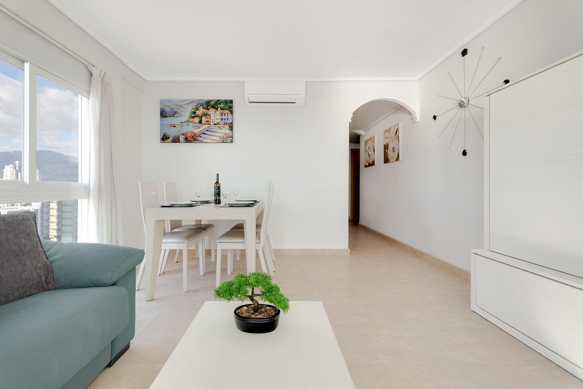 A modern living room with a sofa, dining table, and a bonsai tree.