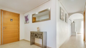 A hallway with a wooden door, a console table with drawers, a large mirror, and framed artwork on the walls. - Brilliant Panoramic Front line apartment Veracruz Levante (R099) (Benidorm)