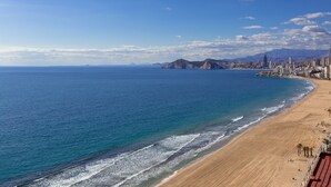 A coastal cityscape with a wide sandy beach, a clear blue sea, and a distant mountain range. - Brilliant Panoramic Front line apartment Veracruz Levante (R099) (Benidorm)