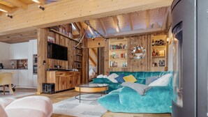 En moderne stue med en tealfarvet sofa, trædetaljer og et køkken, der kan ses igennem en åben dør.
