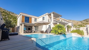 Una moderna casa a due piani con piscina, area salotto esterna e vista sulle colline circostanti.
