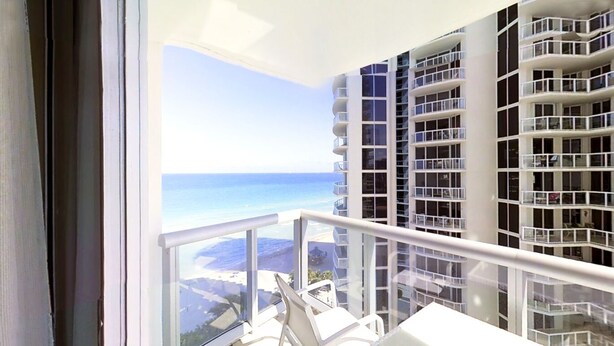 A balcony with a view of the ocean and adjacent high-rise buildings. - Private Beachfront Condominium with Resort and Amenities Access (Sunny Isles Beach)