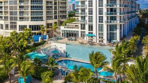 A modern hotel with a large pool, multiple balconies, and lush greenery. - Private Beachfront Condominium with Resort and Amenities Access (Sunny Isles Beach)