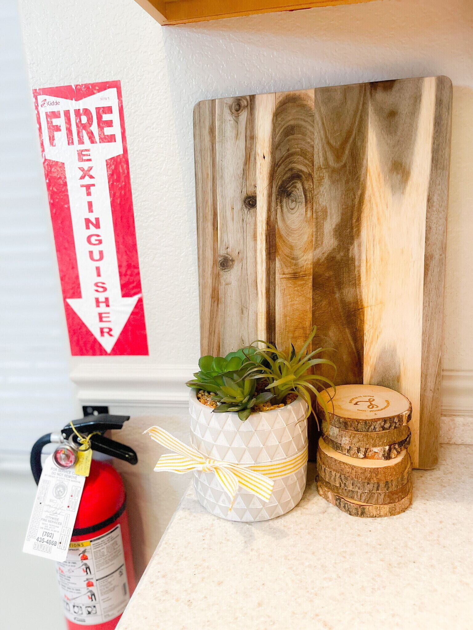 A fire extinguisher, a potted plant, and wooden coasters on a countertop.