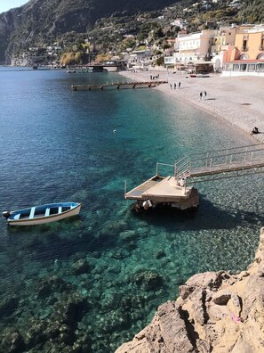 A coastal scene with a clear blue sea, a small boat, and a pier with a platform.