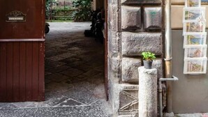 Ein rundbogiger Durchgang führt in einen Innenhof mit einer Steinmauer, einer kleinen Pflanze und einem Schild.