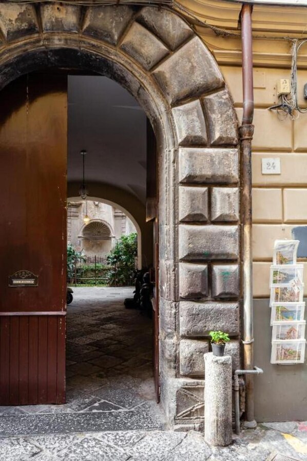 An arched doorway leading to a courtyard with a stone wall, a small plant, and a signboard.
