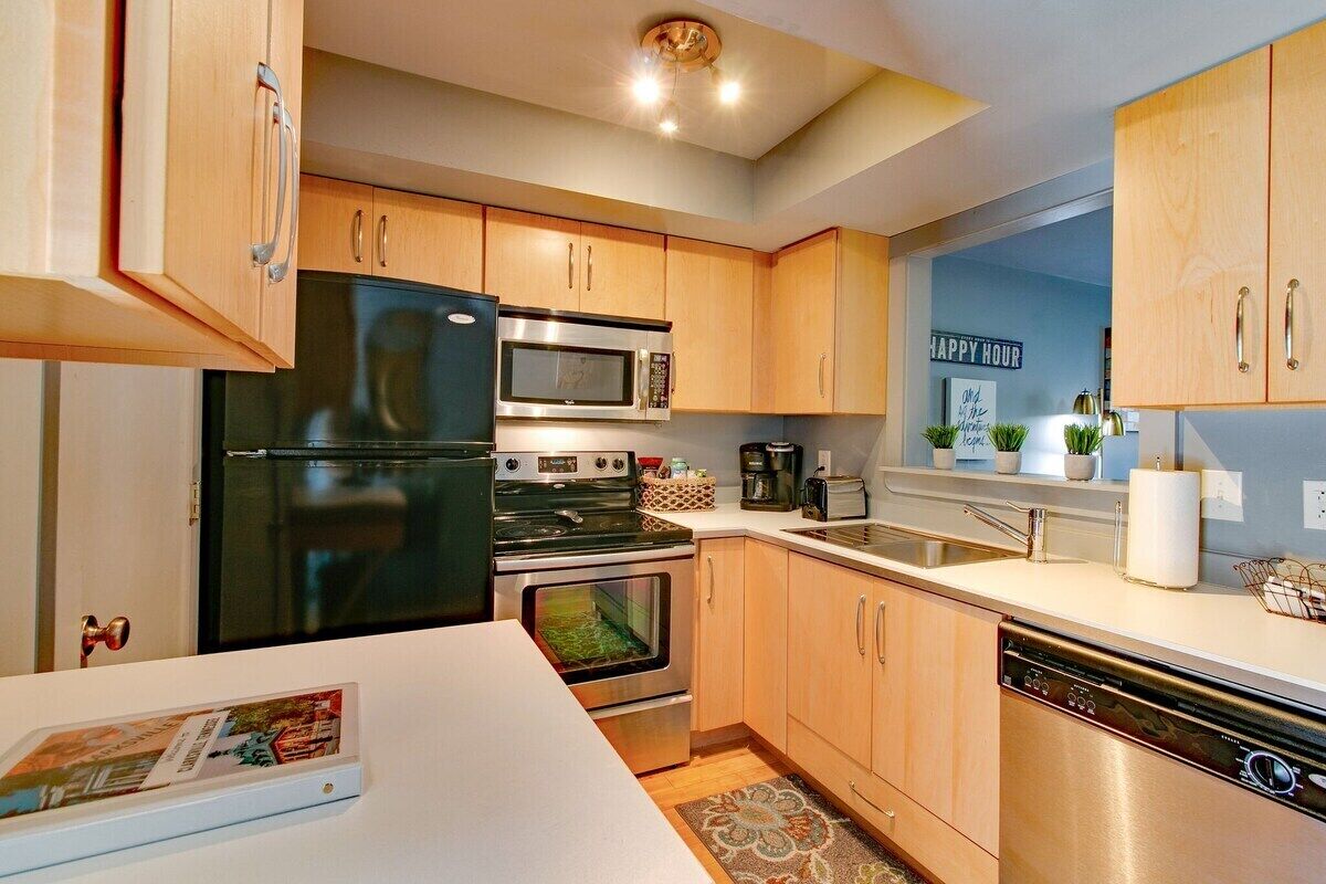 Una cocina moderna con armarios de madera, electrodomésticos de acero inoxidable, lavavajillas y una encimera con fregadero.
