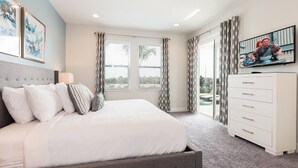 Ein Schlafzimmer mit einem Bett, einem Schminktisch, einem Fernseher und großen Fenstern mit Vorhängen.