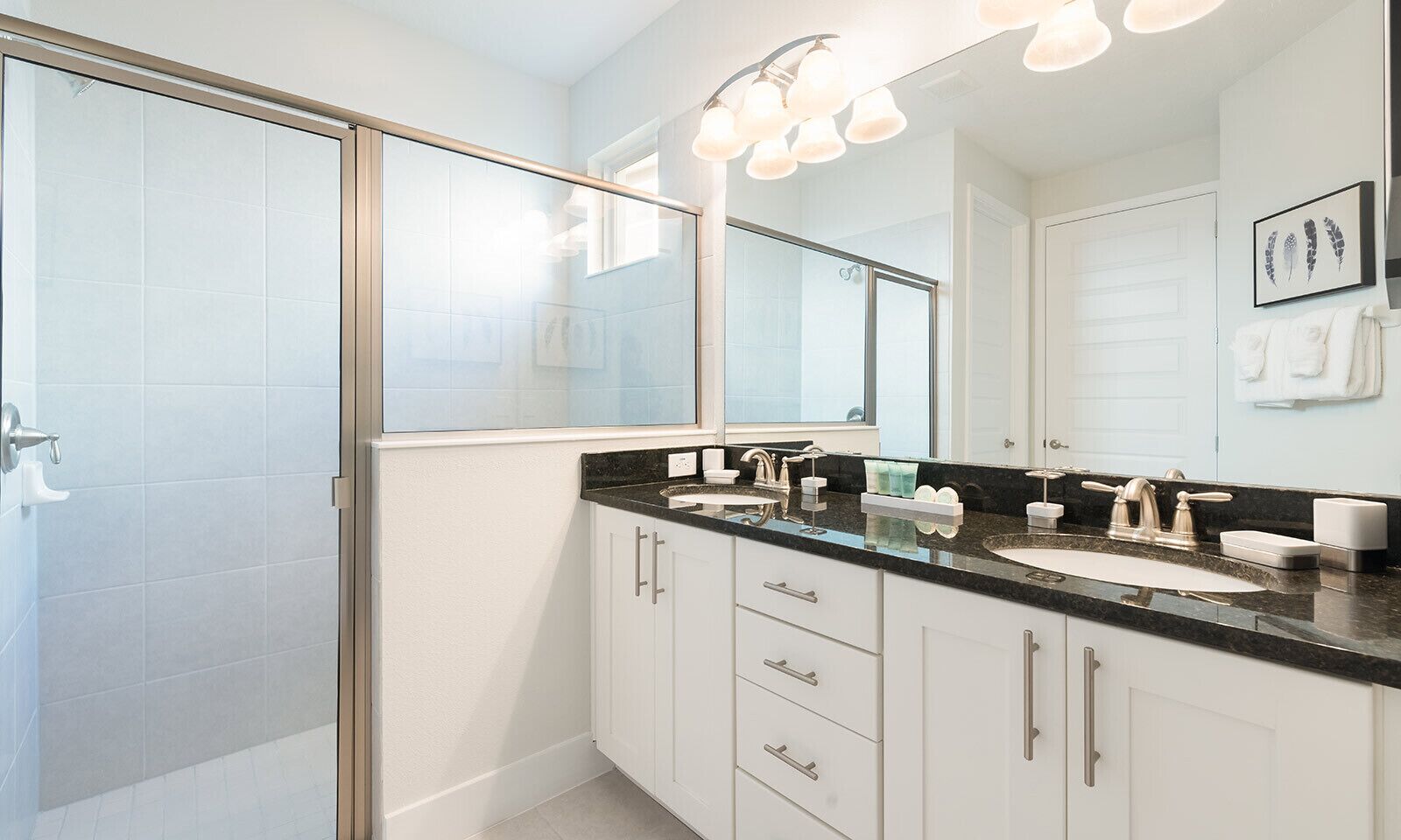 Une salle de bain moderne dotée d’une douche à parois de verre, d’un meuble-lavabo à deux vasques et d’un grand miroir avec éclairage intégré au-dessus.