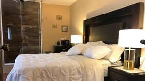 A hotel room with a bed, a nightstand, a lamp, a glass shower enclosure, and a wall with framed pictures. - House of Stairs, Pátzcuaro, Michoacán (Pátzcuaro)