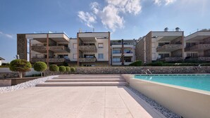 Un immeuble moderne à plusieurs étages, doté de balcons, d’une piscine et d’une façade en pierre.
