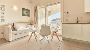 Un salon moderne comprenant un canapé, une table à manger avec des chaises, un coin cuisine avec un évier et une grande fenêtre donnant sur l’extérieur.