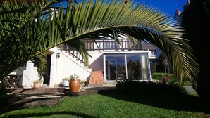 A modern house with a glass door entrance, a small patio with a chair, and a large potted plant in the foreground.