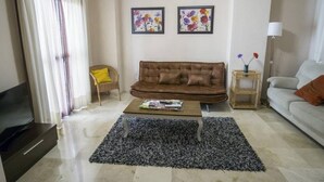 Un salon avec un canapé marron, une table basse, un téléviseur et deux tableaux représentant des motifs floraux, encadrés et accrochés au mur.