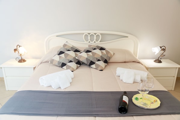 A neatly made bed with a patterned pillow, a rolled towel, and a wine bottle on a tray.