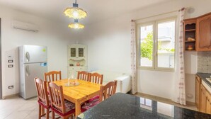 A compact kitchen with a dining table, chairs, a refrigerator, a cabinet, and a window with curtains. - [Beach-Seafront 5 Stars] Comfortable Holiday Home (Avola)