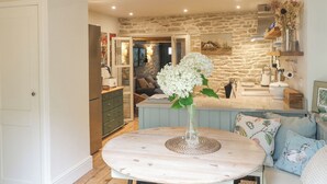 Une cuisine chaleureuse avec un mur en pierre, une table à manger agrémentée d’un vase de fleurs et une vue sur le salon.
