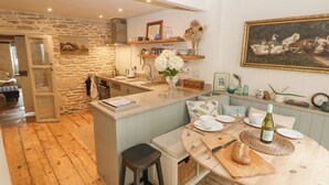 Une cuisine chaleureuse avec un mur en pierre, un plancher en bois et un coin repas doté d’une table ronde.