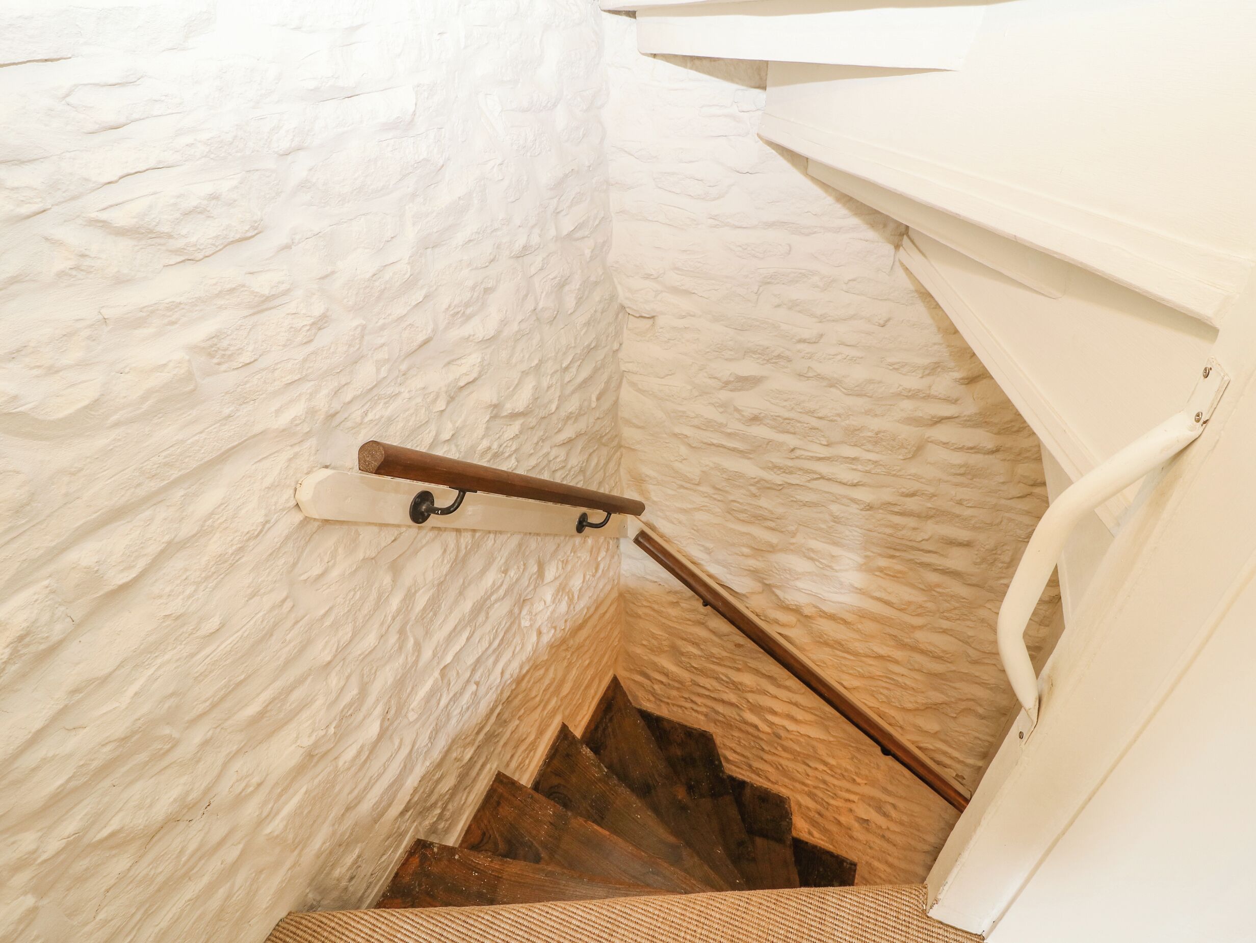 Eine Treppe mit Holzbalken und einem Metallgeländer, die zu einer Zwischenebene mit einer weißen Wand und einem Holzbalken führt.