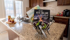A kitchen with granite countertops, wooden cabinets, and a stainless steel range hood. There are two cookbooks on the counter, and a coffee maker is visible on the right side. - 🍷 Luxury Pond House, 10 minutes to Niagara Falls (Thorold)