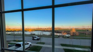 A view through a window of a parking lot with a white SUV, a truck, and a car parked. There is a grassy area with a small pond and a field in the background. - 🍷 Luxury Pond House, 10 minutes to Niagara Falls (Thorold)
