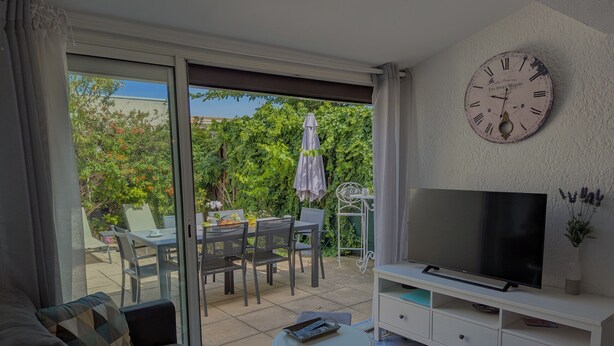 A modern living room with a sofa, TV, and a dining area with chairs and a table. - Sol-y-Days Grau Village, Holiday home with large terrace (Le Grau-du-Roi)