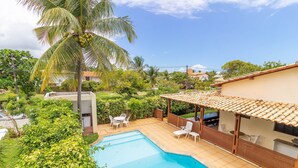 A swimming pool with a tiled deck, surrounded by lush greenery and a covered patio area with outdoor furniture.