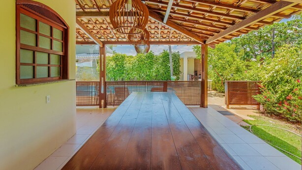 An open wooden deck with a tiled floor, a hanging light fixture, and a view of greenery outside.