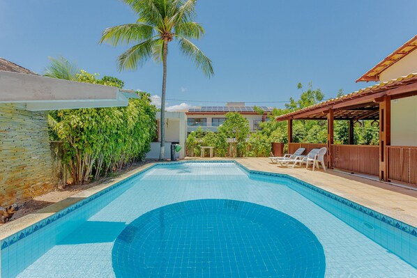 A swimming pool with a tiled edge, surrounded by greenery and a wooden pergola. - GB44 Casa 4 Quartos a 200m da Praia (Camaçari)