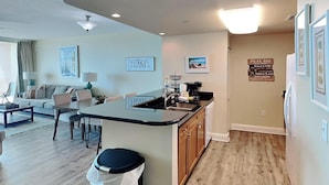 A modern living room with a sofa, coffee table, and a dining area with a kitchen island. - Aqua #404 by Resort Collection (Panama City Beach)