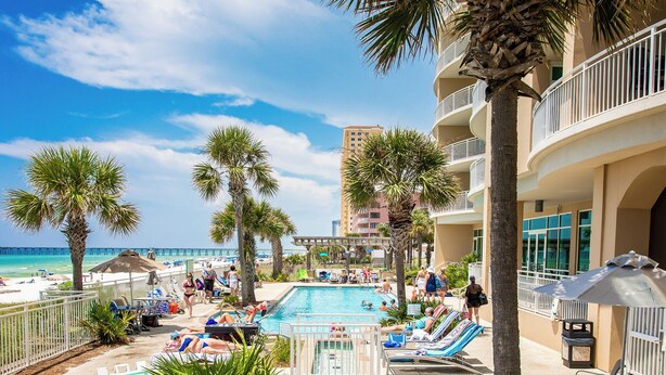 A pool area with lounge chairs and palm trees, overlooking a beach and ocean. - Aqua #404 by Resort Collection (Panama City Beach)
