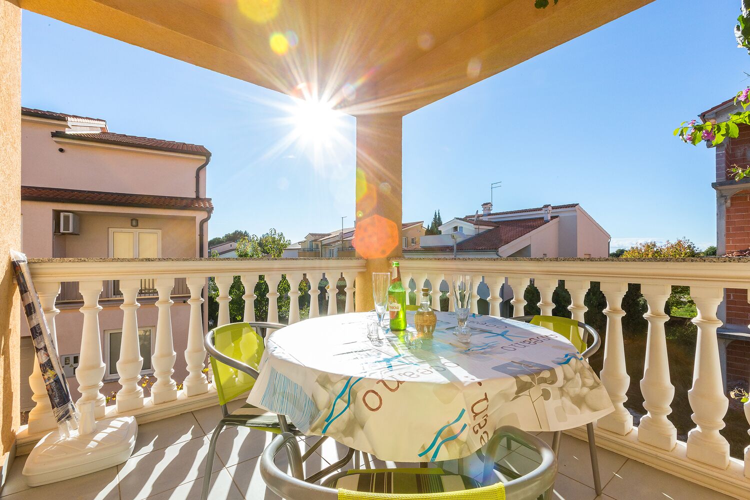 A balcony with a round table, chairs, and a sun shining through the balustrade.