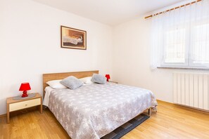 Ein Schlafzimmer mit einem hölzernen Bett, zwei Nachttischen mit Lampen, einem gerahmten Bild an der Wand und einem Fenster mit Jalousien.