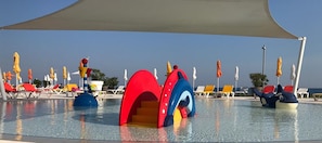 Zona de piscina con estructuras de juego coloridas, tumbonas y sombrillas.