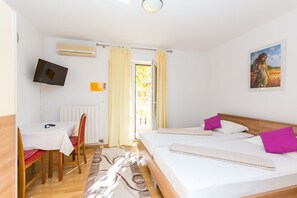 Quarto de hotel com cama, escrivaninha, cadeira, televisão e um quadro na parede.