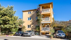 Un edificio residencial de varios pisos con balcones, coches aparcados y vegetación circundante.