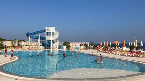 Una piscina con tobogán de agua, sillas de descanso y sombrillas.