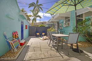 A patio with a table and chairs, a striped umbrella, and a pool table. - Spacious Beach Bungalow: Steps to Beach & Downtown (Lake Worth)