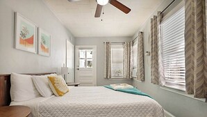 Une chambre à coucher avec un lit, un ventilateur de plafond, une fenêtre avec des stores et une porte.