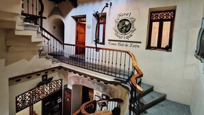 A multi-level interior with a staircase, a decorative wall with a 'Hotel Boutique Casa Cid de León' sign, and a small window with a decorative grille. - Boutique Hotel Casa Cid de León (Oaxaca)