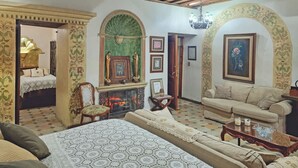A cozy living room with a fireplace, a sofa, a dining table, and a bed with a patterned bedspread. - Boutique Hotel Casa Cid de León (Oaxaca)