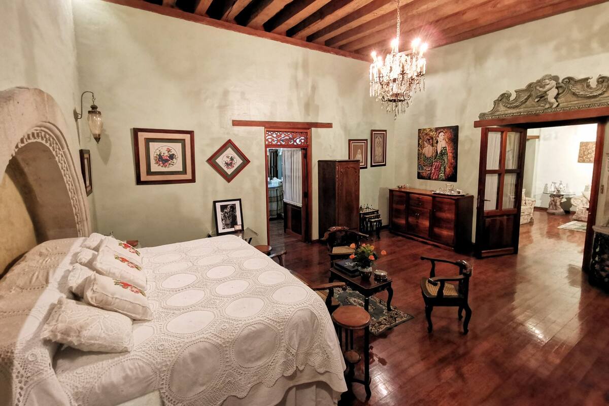 A spacious room with a large bed, wooden ceiling beams, a chandelier, and a wooden cabinet.