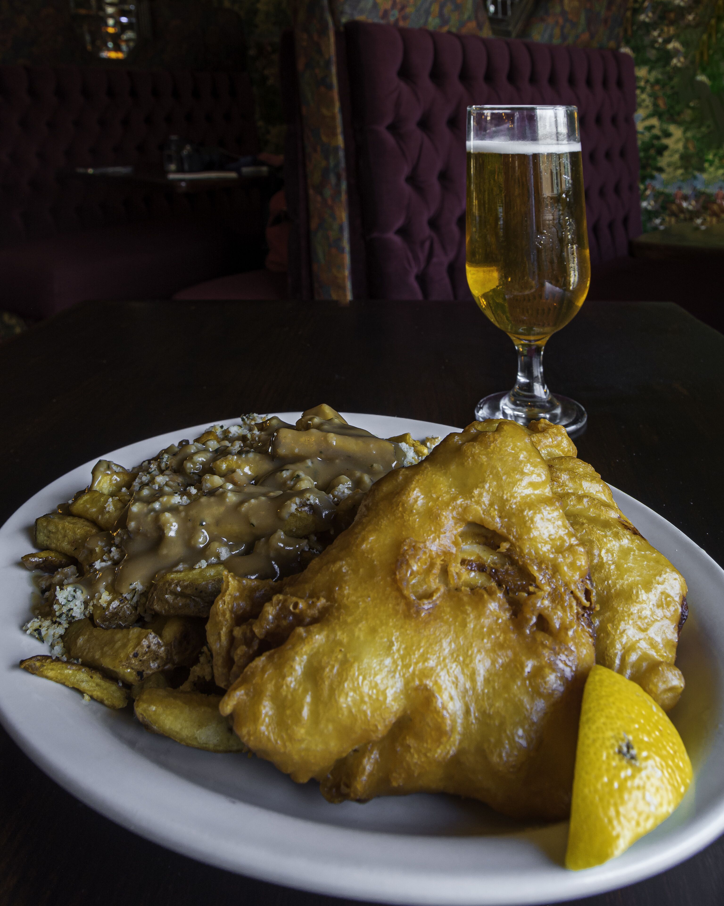 A plate of fish and chips with a glass of beer on a table in a restaurant.