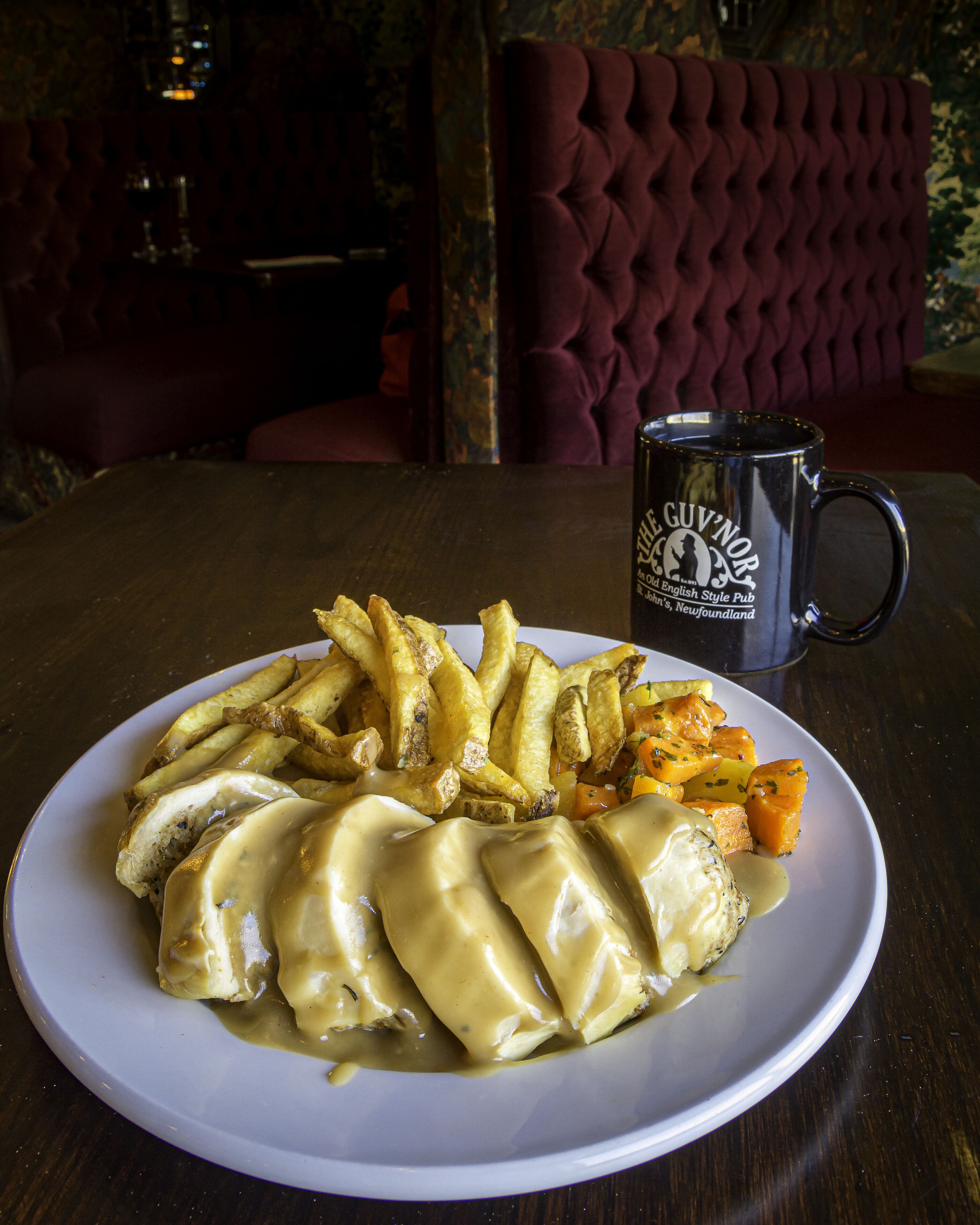 A plate of food with gravy, a beer mug, and a red upholstered chair in the background.