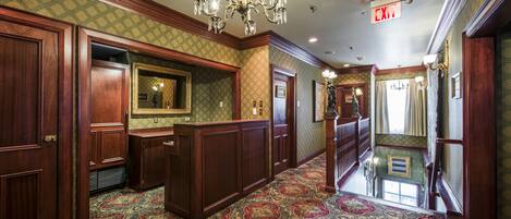 A hallway with patterned carpet, wooden paneling, a chandelier, and an exit sign.